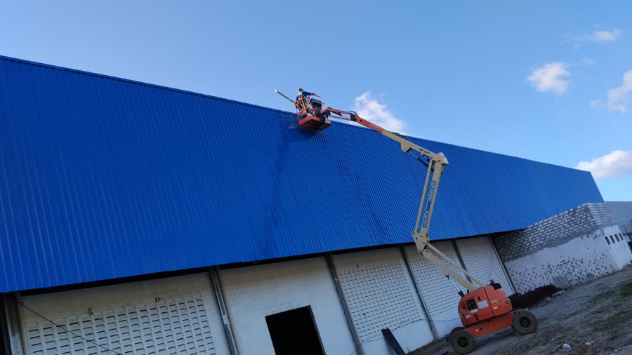 Trabalhador em plataforma elevatória sobre telhado metálico industrial contra o céu