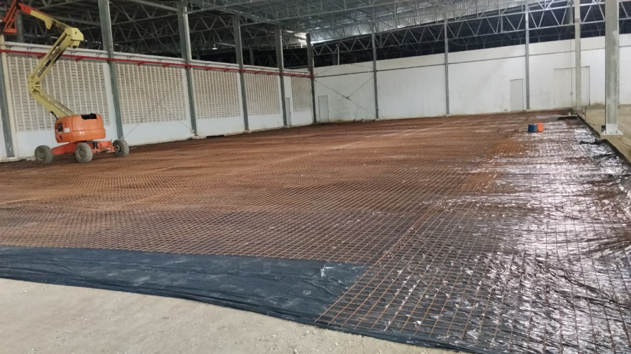 Ferragem de piso armado em primeiro plano com estrutura metálica ao fundo, obra civil e metálica integradas