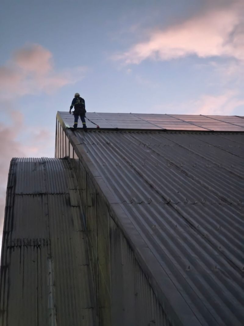 Técnico ancorado em cobertura industrial ao entardecer, sistema de segurança conforme NR-35