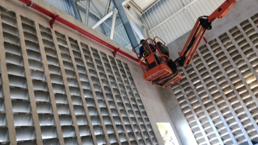 Trabalhador em plataforma elevatória realizando manutenção em painel industrial