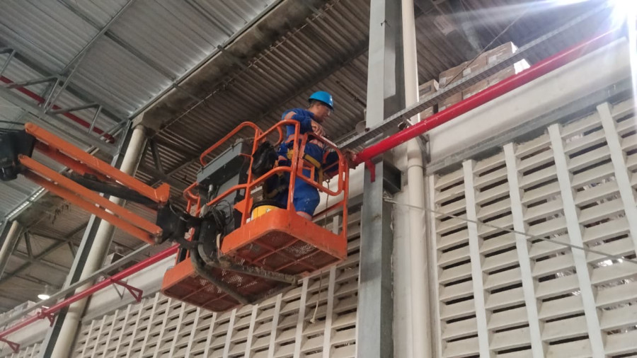 Técnico em plataforma elevatória instalando tubulação de combate a incêndio na cobertura de galpão industrial
