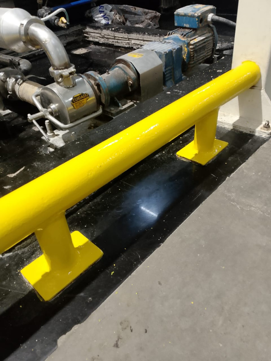 Barreira de proteção amarela sobre postes fixados ao piso industrial, segurança de máquinas conforme NR-12