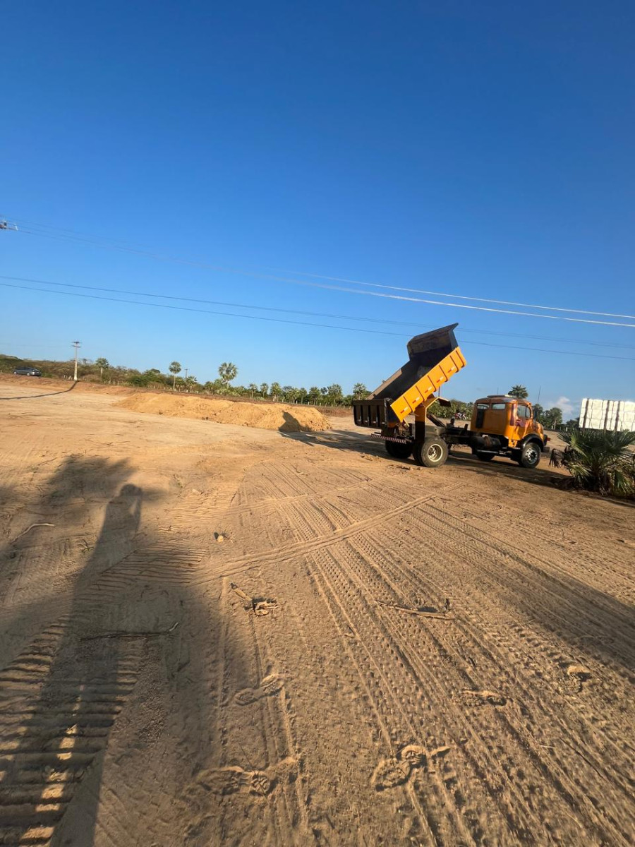 Caminhão basculante descarregando terra ao amanhecer, terreno nivelado em obra de terraplenagem