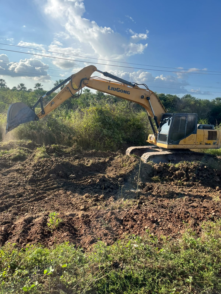 Escavadeira Engemec limpando vegetação em contraluz ao entardecer, serviço de terraplenagem