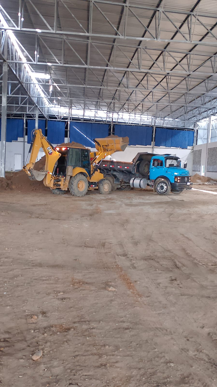 Retroescavadeira carregando caminhão com terra dentro de galpão industrial em construção